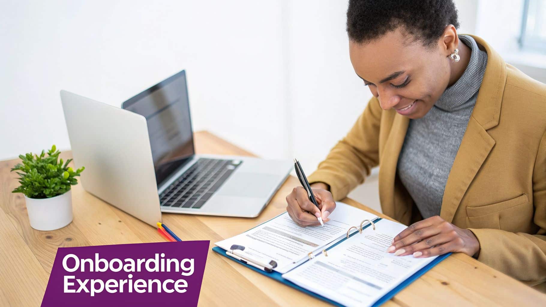 Smiling Black woman writing in a binder at a desk with a laptop and 'Onboarding Experience' text.