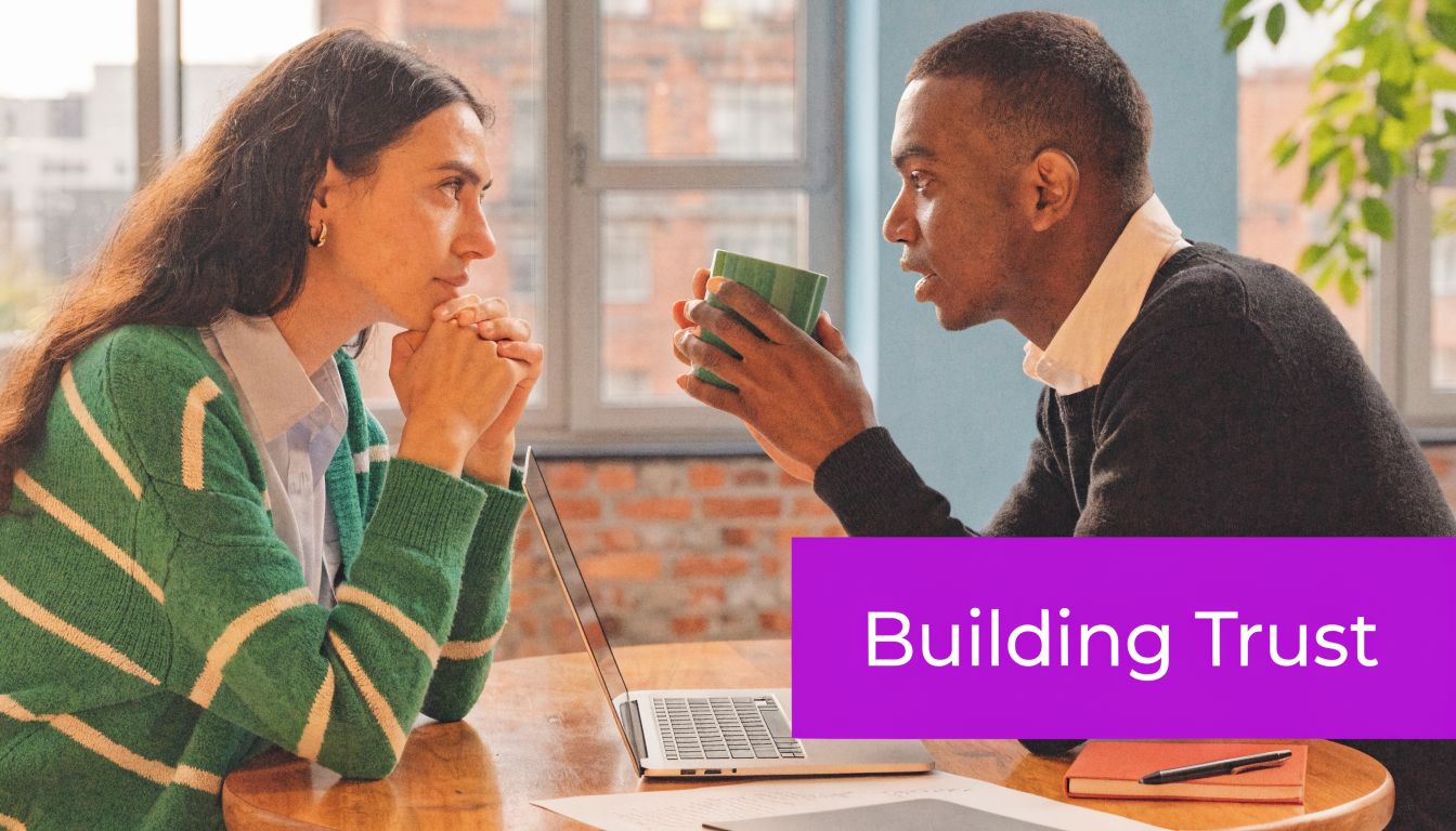 A woman and a man talking during a business meeting while sitting at a table with a laptop.